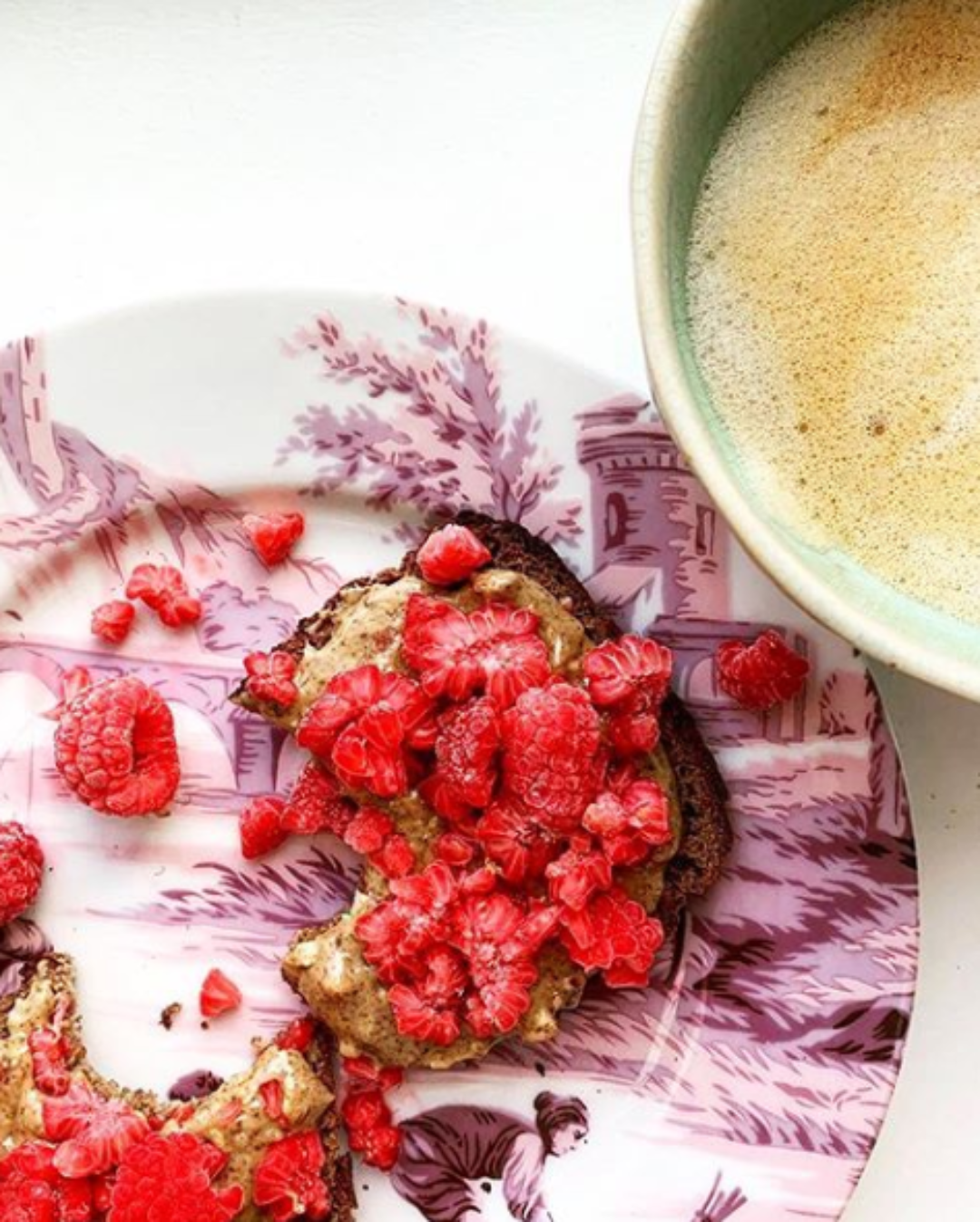 Toast with raspberries on a decorative plate next to a cup of coffee.
