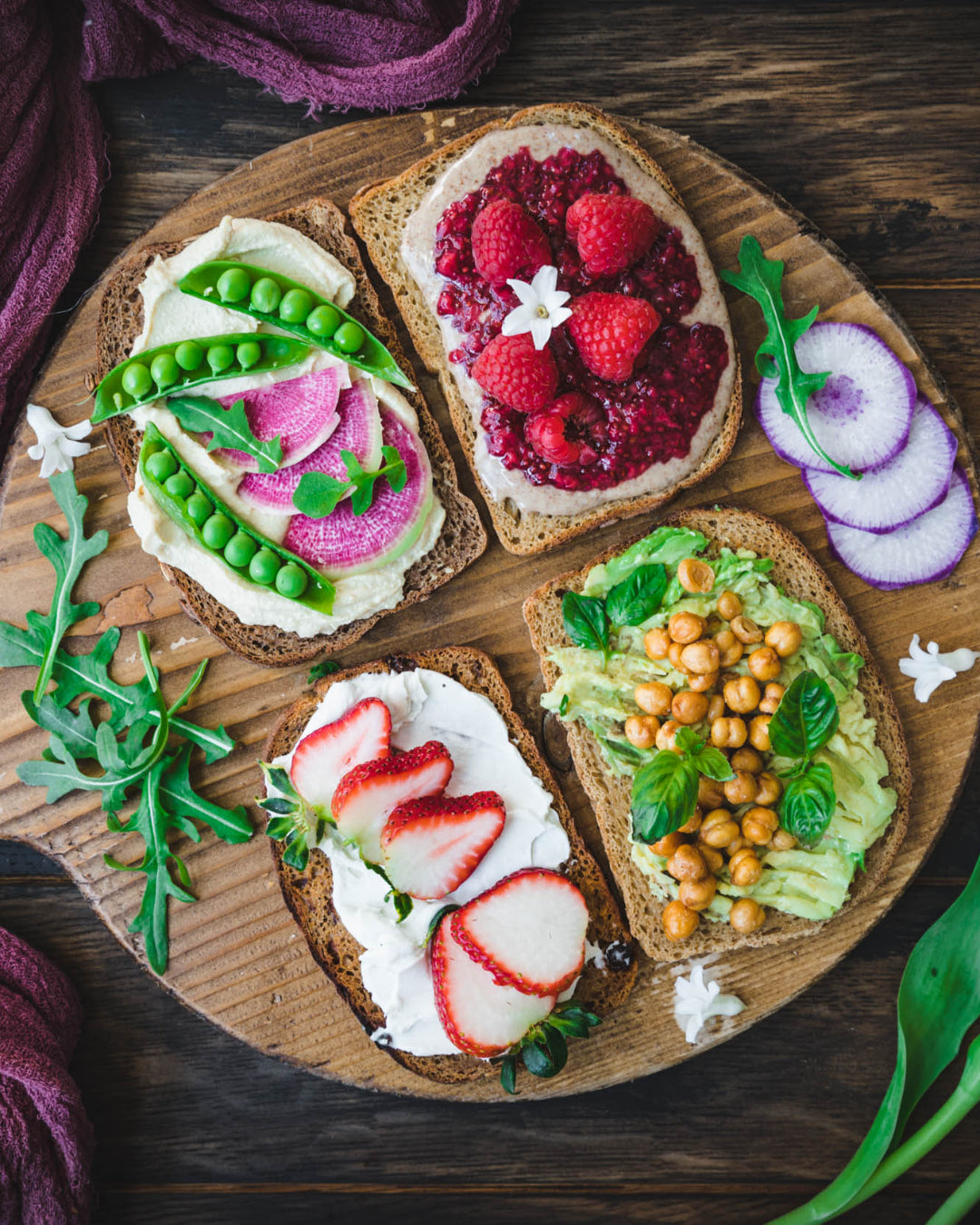 Four slices of bread with different toppings on a wooden board, surrounded by purple yarn and tulips.