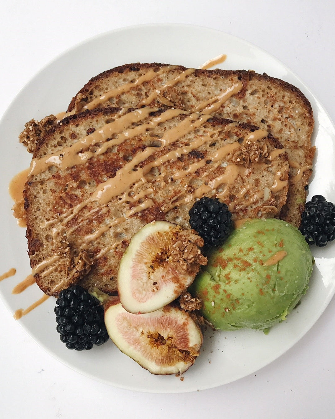 Plated dish with toast, figs, blackberries, and green ice cream on a white background