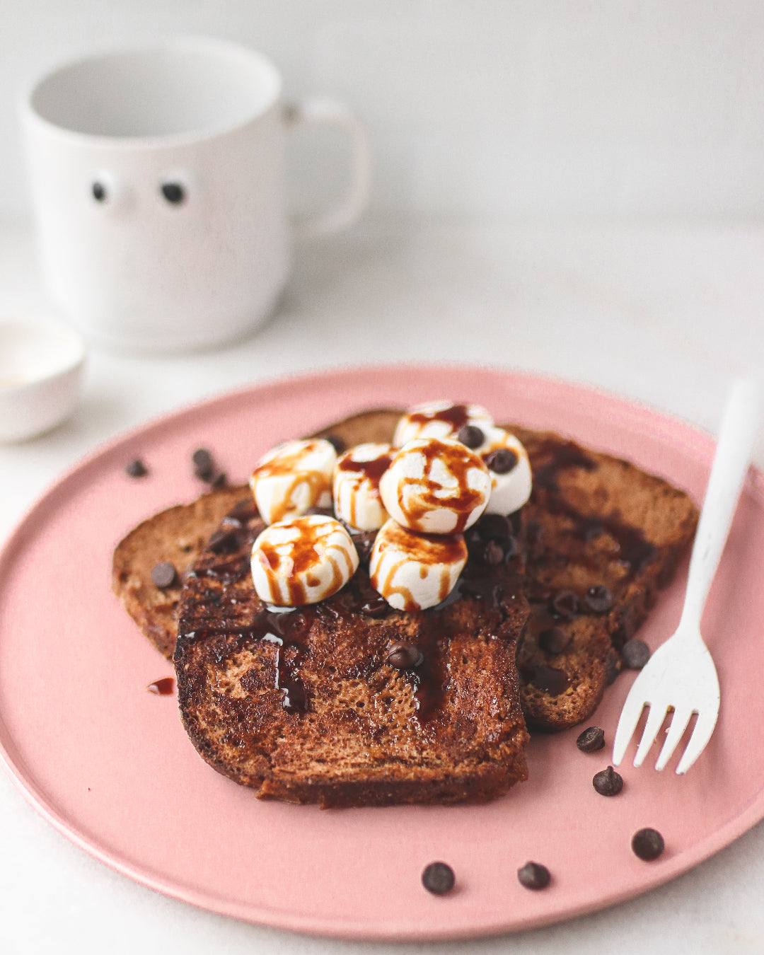 French toast with syrup and whipped cream on a pink plate with a white mug in the background.
