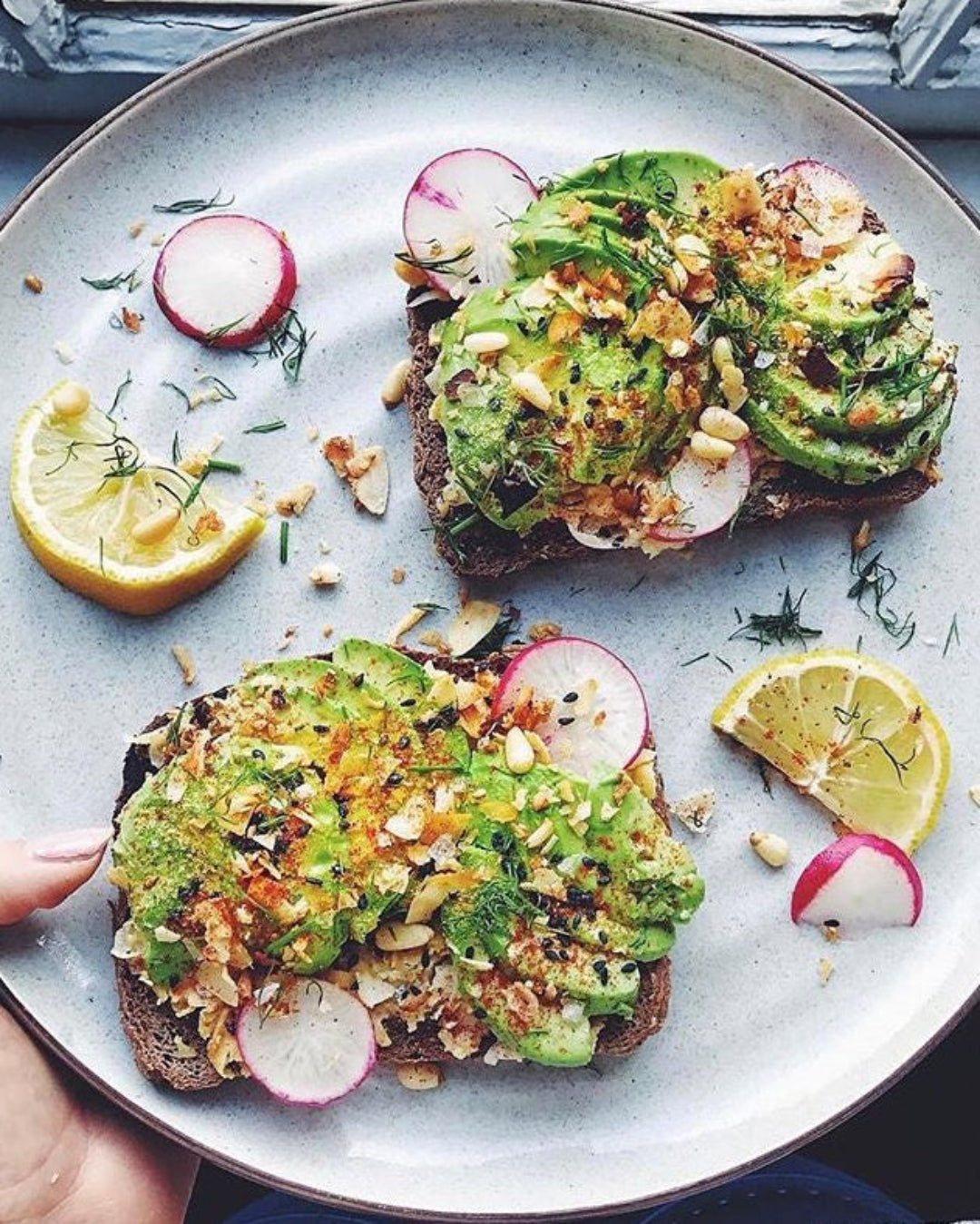 Avocado toast with radishes and lemon wedges on a plate.