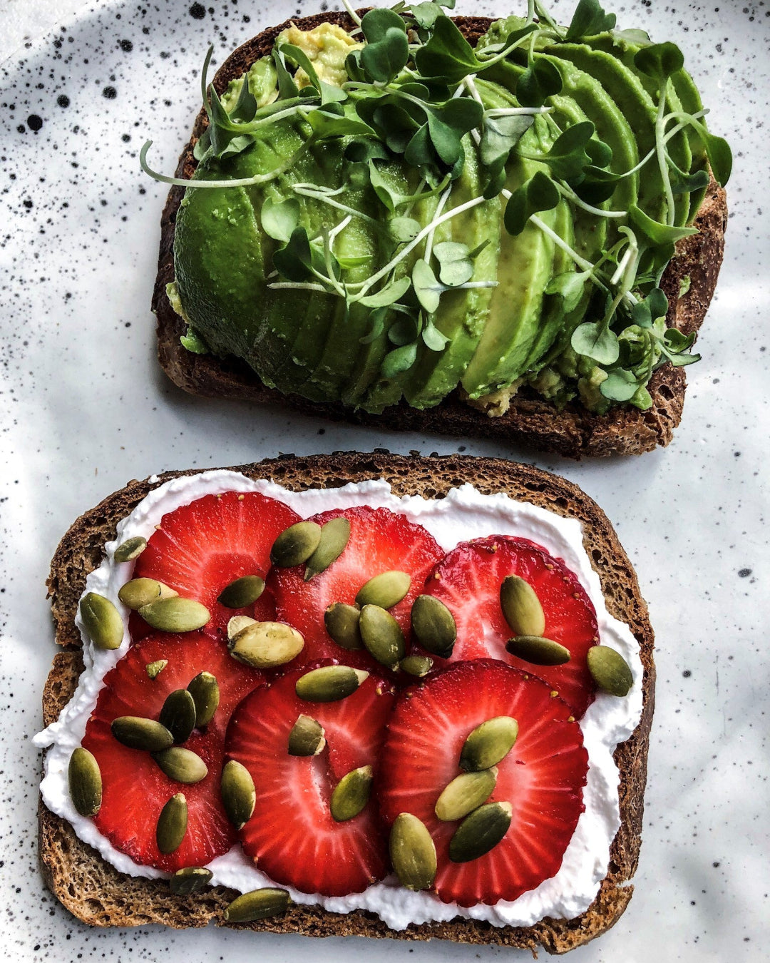 Two slices of toast with avocado and greens on top, and strawberries and cream on the bottom slice.